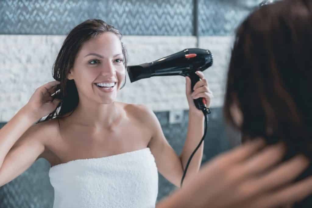 Mulher Secando Cabelo em Frente ao Espelho Sorrindo