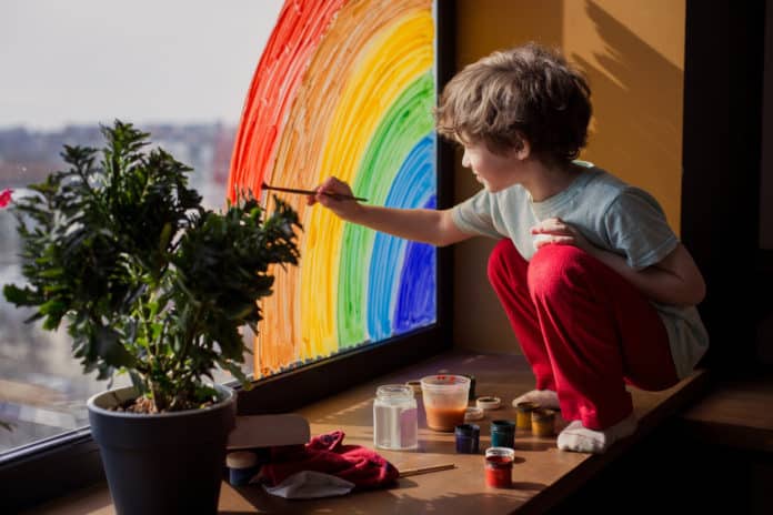 Criança pintando um arco-íris na janela.