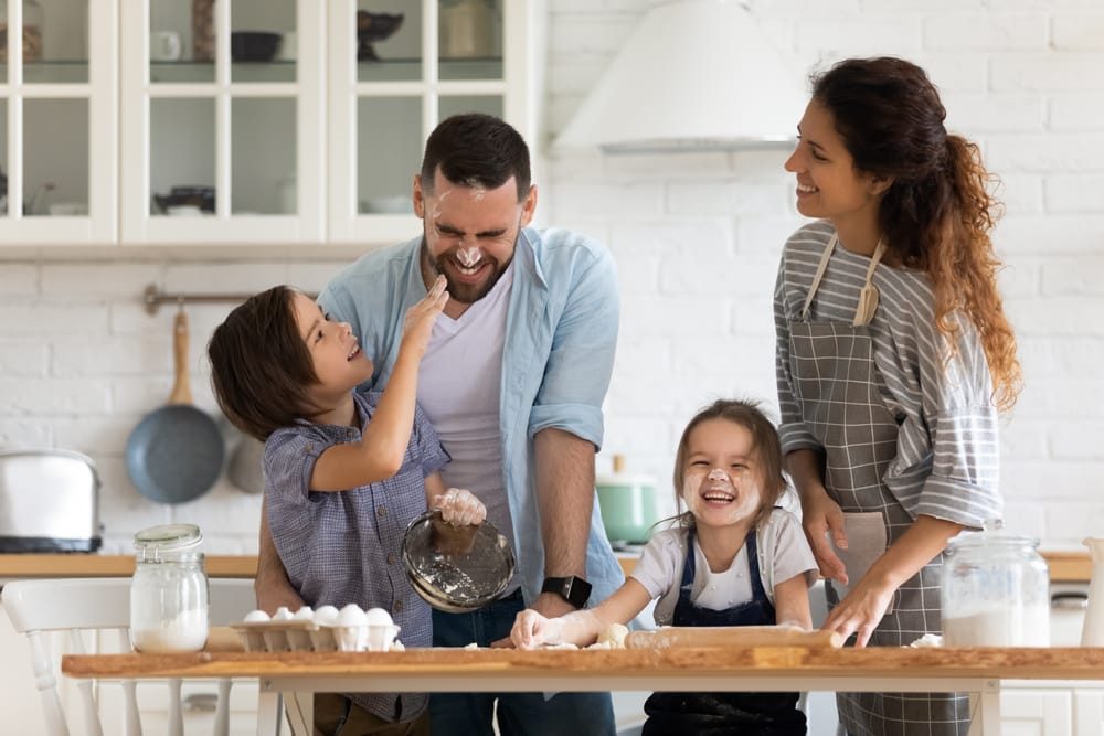 Família reunida na cozinha ensinando os filhos a cozinhar.