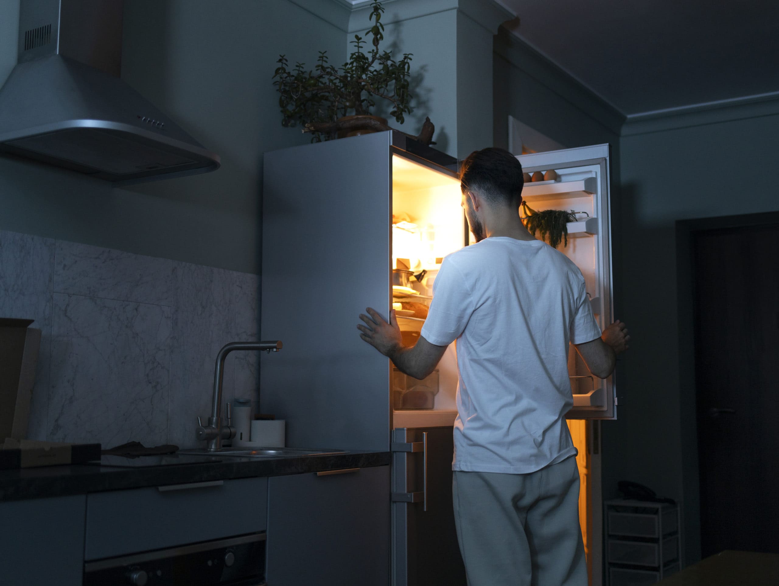Homem abrindo geladeira inox procurando lanche.